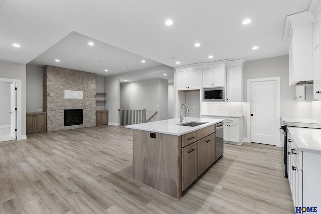 kitchen featuring sink, a stone fireplace, a kitchen island with sink, white cabinets, and appliances with stainless steel finishes