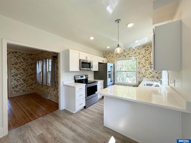 kitchen featuring kitchen peninsula, appliances with stainless steel finishes, light wood-type flooring, sink, and white cabinetry