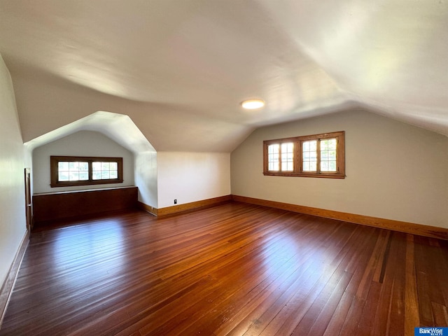 additional living space with dark hardwood / wood-style flooring, a healthy amount of sunlight, and vaulted ceiling