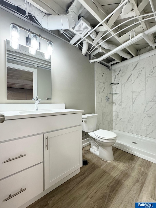 bathroom with tiled shower, hardwood / wood-style floors, vanity, and toilet