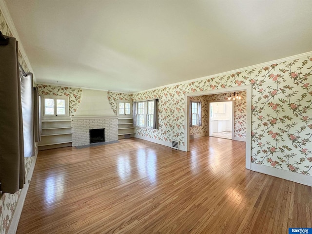 unfurnished living room with hardwood / wood-style floors, a brick fireplace, crown molding, and a healthy amount of sunlight