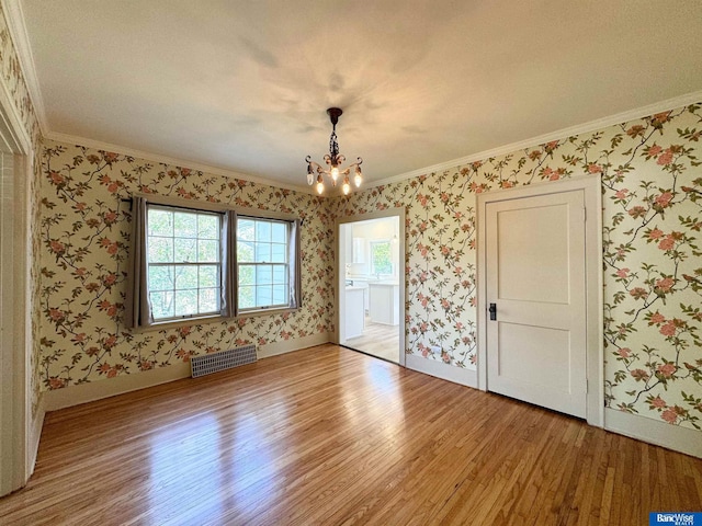 empty room with hardwood / wood-style flooring, ornamental molding, and an inviting chandelier