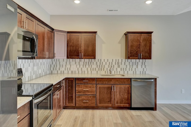 kitchen with backsplash, sink, light wood-type flooring, appliances with stainless steel finishes, and light stone counters