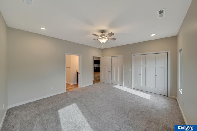 unfurnished bedroom with ceiling fan, two closets, light colored carpet, and ensuite bath