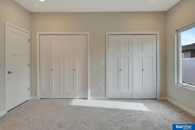 unfurnished bedroom featuring light carpet and multiple closets