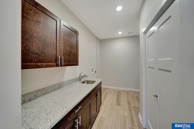 kitchen with light wood-type flooring, light stone countertops, sink, and dark brown cabinetry