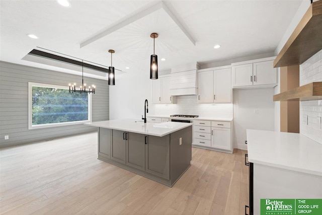 kitchen featuring stainless steel gas stovetop, decorative light fixtures, white cabinetry, and a kitchen island with sink