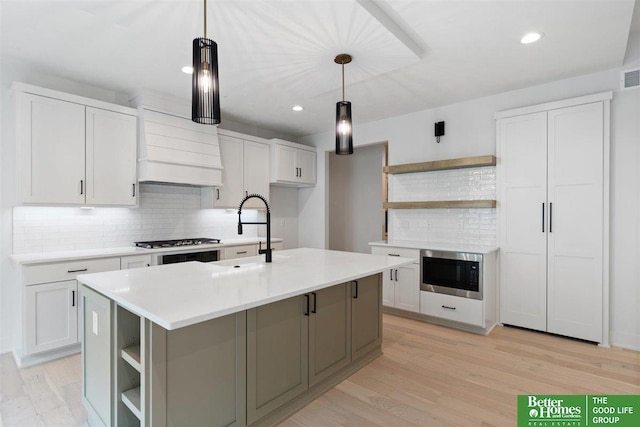 kitchen featuring decorative light fixtures, sink, white cabinetry, and a kitchen island with sink