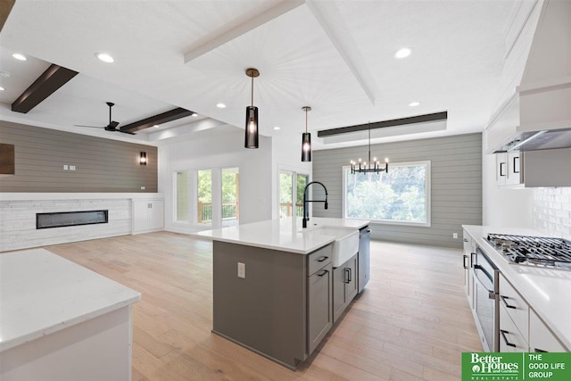 kitchen with ceiling fan with notable chandelier, a kitchen island with sink, pendant lighting, beamed ceiling, and white cabinets