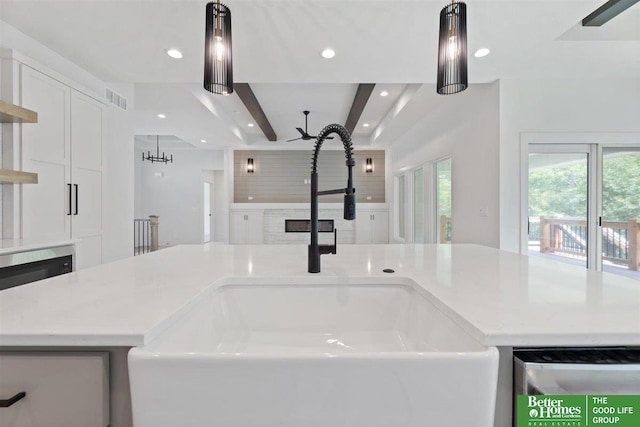 interior details with an island with sink, white cabinetry, hanging light fixtures, and sink