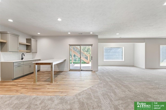 kitchen featuring a textured ceiling, backsplash, light colored carpet, and sink