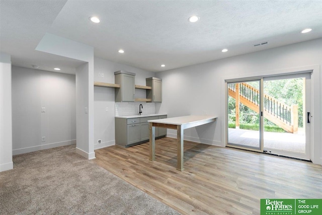 kitchen with sink, light hardwood / wood-style flooring, a textured ceiling, gray cabinets, and decorative backsplash