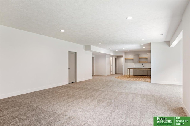 unfurnished living room with a textured ceiling, light colored carpet, and sink