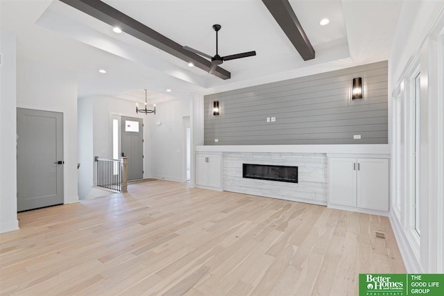 unfurnished living room featuring ceiling fan with notable chandelier, beam ceiling, light wood-type flooring, and a raised ceiling