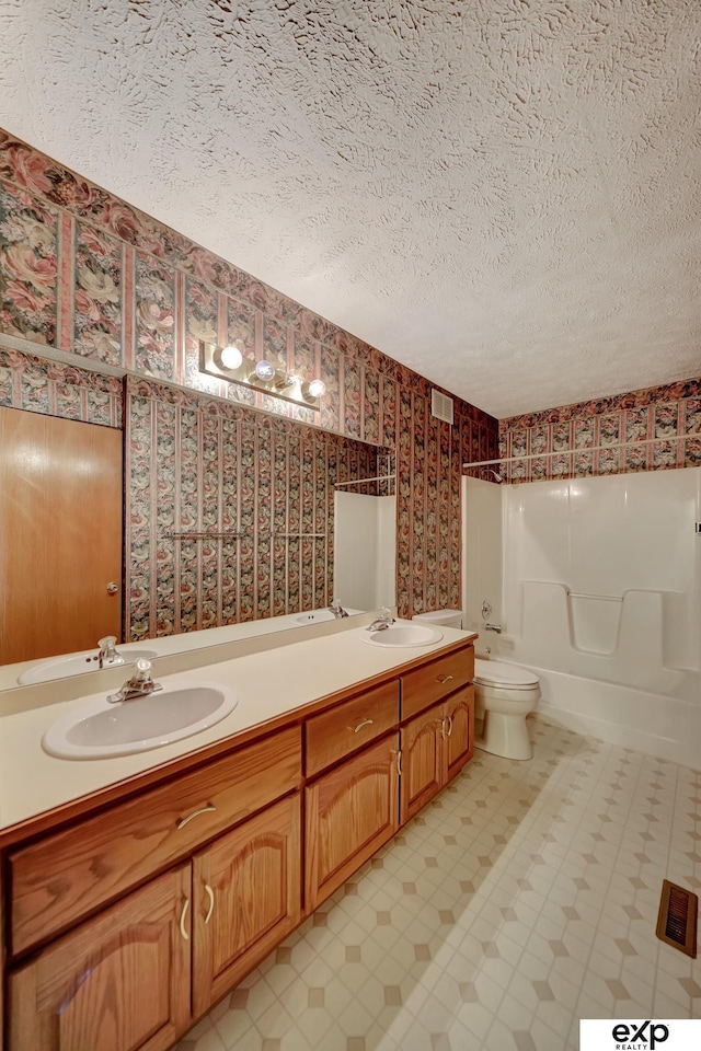 full bathroom featuring toilet, vanity, a textured ceiling, and tub / shower combination