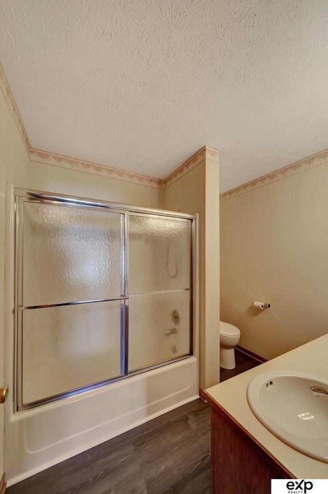 full bathroom featuring vanity, bath / shower combo with glass door, toilet, a textured ceiling, and wood-type flooring