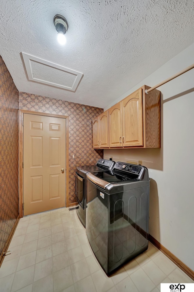 clothes washing area with washer and clothes dryer, cabinets, and a textured ceiling