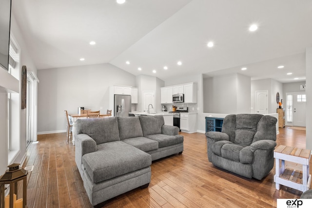 living room with light wood-type flooring, sink, and vaulted ceiling