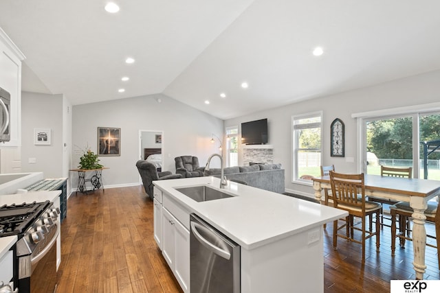 kitchen featuring stainless steel appliances, sink, white cabinets, a stone fireplace, and an island with sink