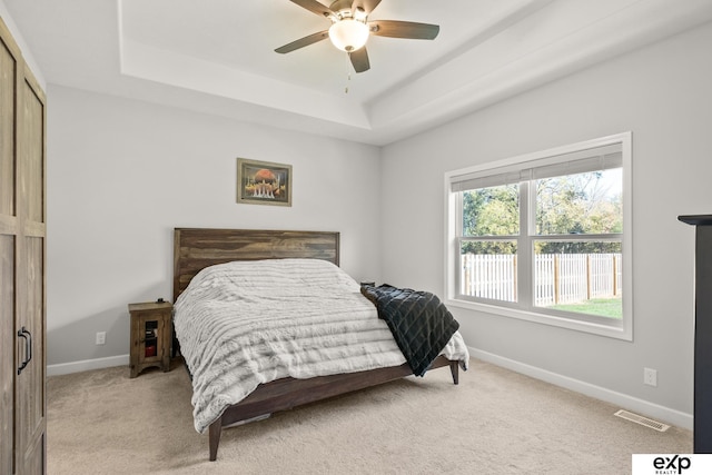 carpeted bedroom featuring a raised ceiling, ceiling fan, and a closet