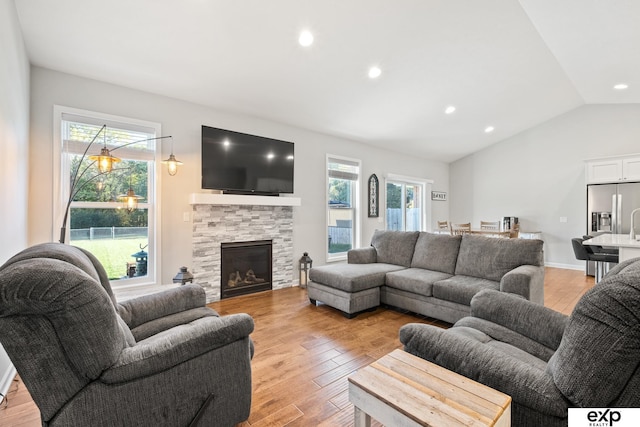 living room with a fireplace, lofted ceiling, light wood-type flooring, and a healthy amount of sunlight