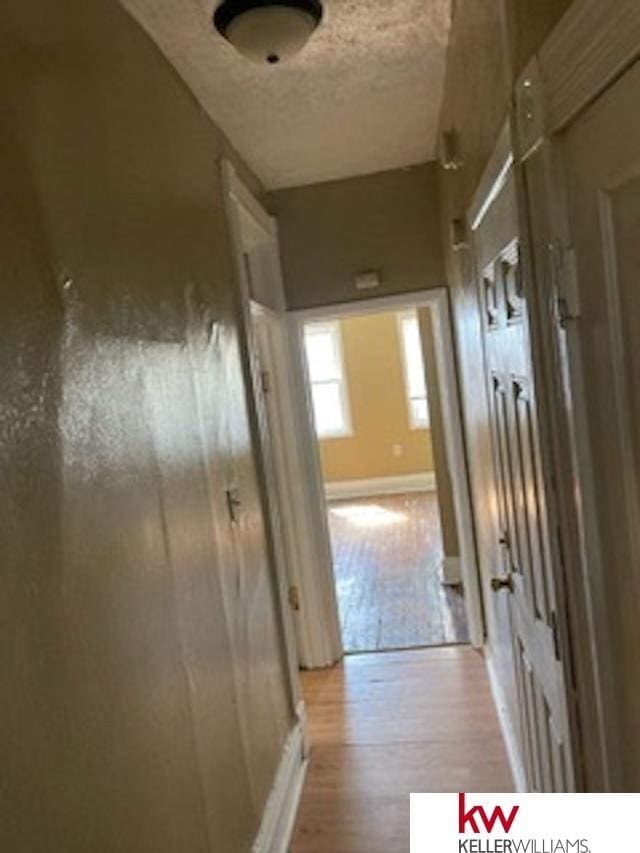 corridor with a textured ceiling and light hardwood / wood-style flooring