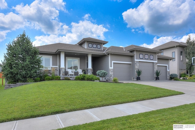 prairie-style home featuring a front lawn, covered porch, and a garage