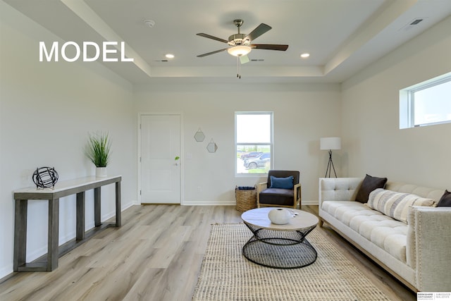 living room featuring ceiling fan, light wood-type flooring, and a tray ceiling