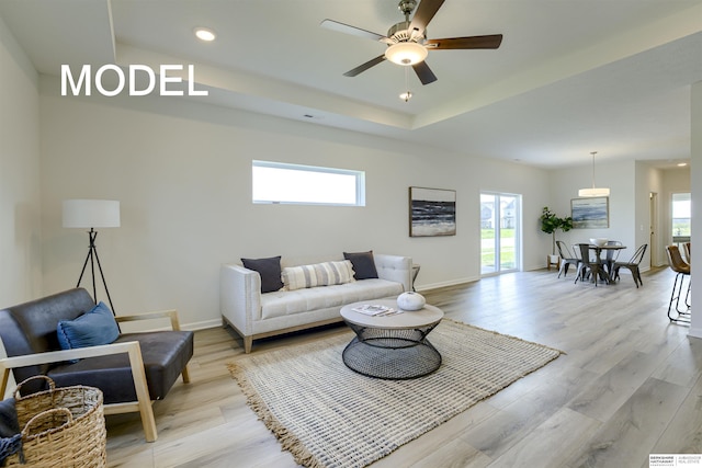 living room with a raised ceiling, ceiling fan, and light wood-type flooring