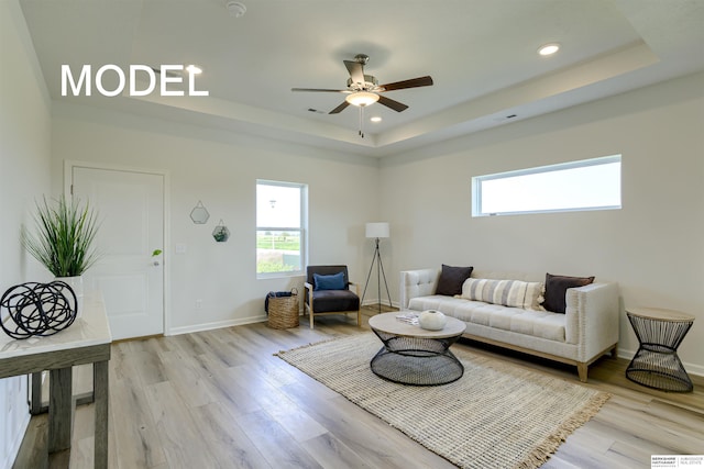 living room with ceiling fan, a healthy amount of sunlight, a raised ceiling, and light hardwood / wood-style flooring