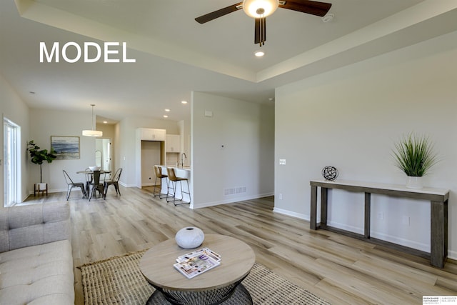 living room with a tray ceiling, light hardwood / wood-style flooring, and ceiling fan