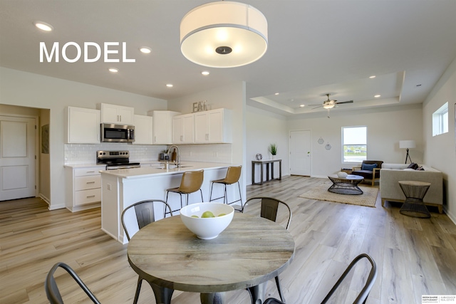 dining space with a raised ceiling, ceiling fan, sink, and light wood-type flooring