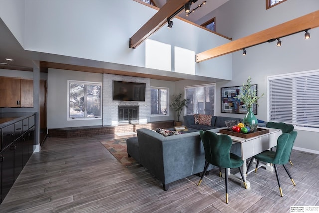 living room featuring track lighting, wood-type flooring, a towering ceiling, and a brick fireplace