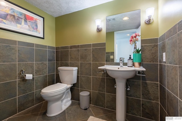 bathroom with tile patterned floors, a textured ceiling, toilet, and tile walls