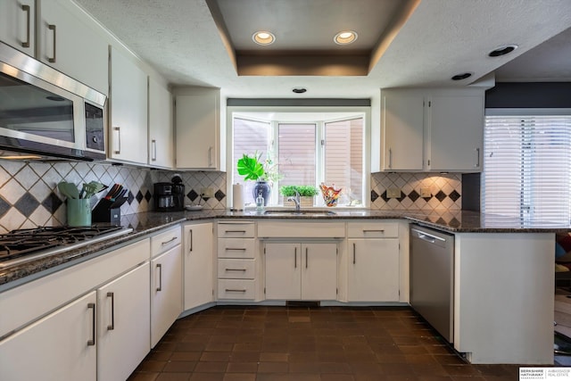 kitchen featuring dark stone counters, a raised ceiling, decorative backsplash, appliances with stainless steel finishes, and white cabinetry