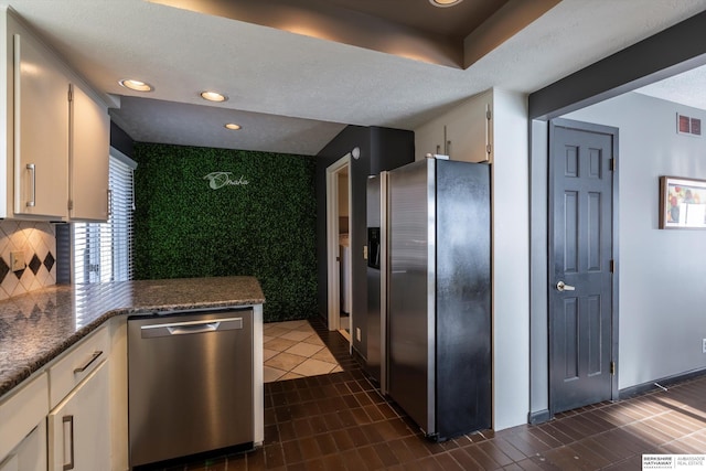 kitchen featuring white cabinetry, stainless steel appliances, tasteful backsplash, dark stone counters, and dark tile patterned flooring