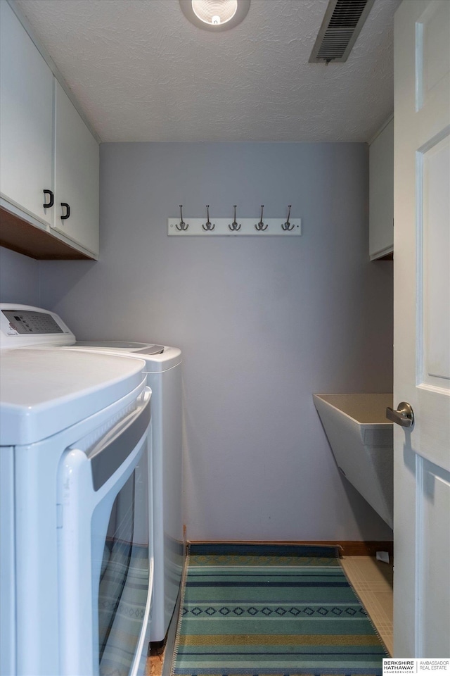 laundry room featuring washer and clothes dryer, cabinets, and a textured ceiling