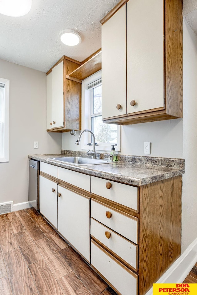 kitchen featuring stainless steel dishwasher, a textured ceiling, sink, light hardwood / wood-style floors, and white cabinetry