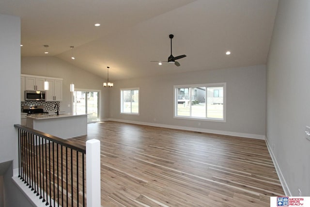 unfurnished living room with ceiling fan with notable chandelier, light hardwood / wood-style flooring, and high vaulted ceiling