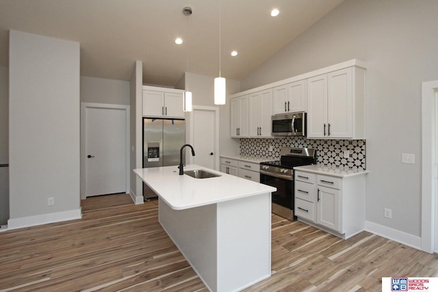 kitchen with pendant lighting, sink, appliances with stainless steel finishes, white cabinets, and a center island with sink