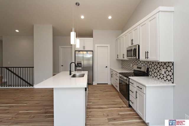 kitchen with pendant lighting, white cabinetry, stainless steel appliances, tasteful backsplash, and an island with sink