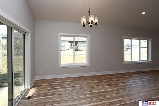 spare room featuring an inviting chandelier, plenty of natural light, and dark hardwood / wood-style floors