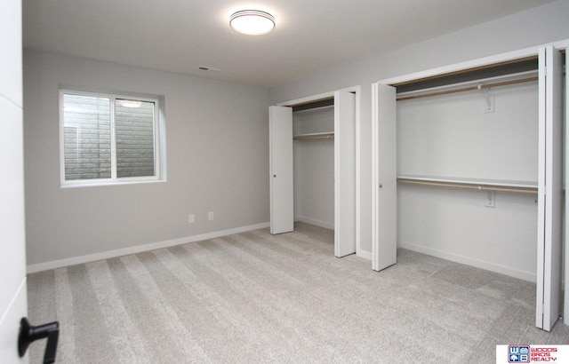 unfurnished bedroom featuring light colored carpet and two closets