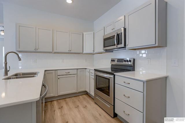 kitchen featuring gray cabinetry, sink, stainless steel appliances, light hardwood / wood-style flooring, and decorative backsplash