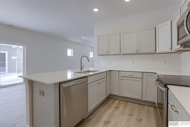 kitchen featuring a wealth of natural light, sink, stainless steel appliances, kitchen peninsula, and light wood-type flooring