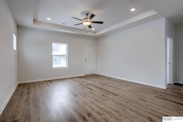 unfurnished room with ceiling fan, wood-type flooring, and a tray ceiling