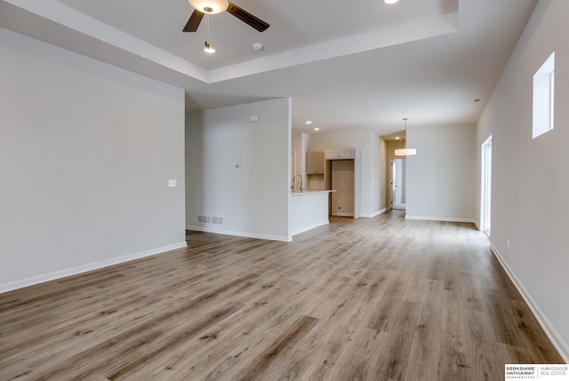 unfurnished living room with a tray ceiling, ceiling fan, and light hardwood / wood-style floors