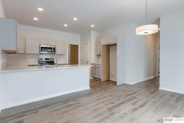 kitchen featuring pendant lighting, sink, appliances with stainless steel finishes, tasteful backsplash, and light hardwood / wood-style floors