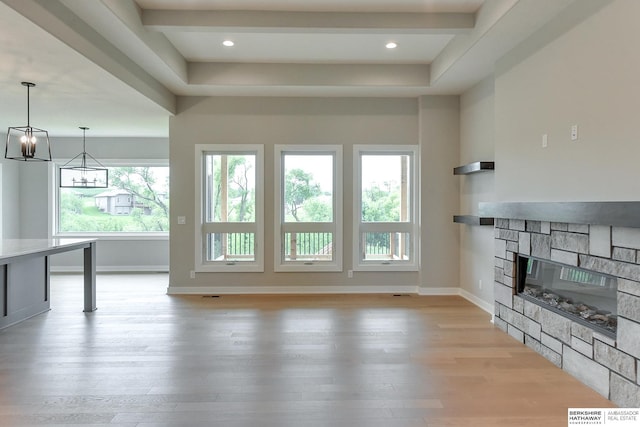 unfurnished living room featuring a notable chandelier, beamed ceiling, a stone fireplace, and light hardwood / wood-style floors