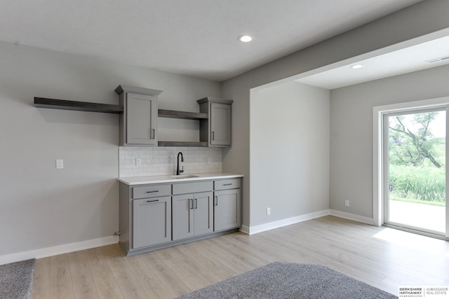 kitchen with sink, gray cabinetry, light wood-type flooring, and decorative backsplash